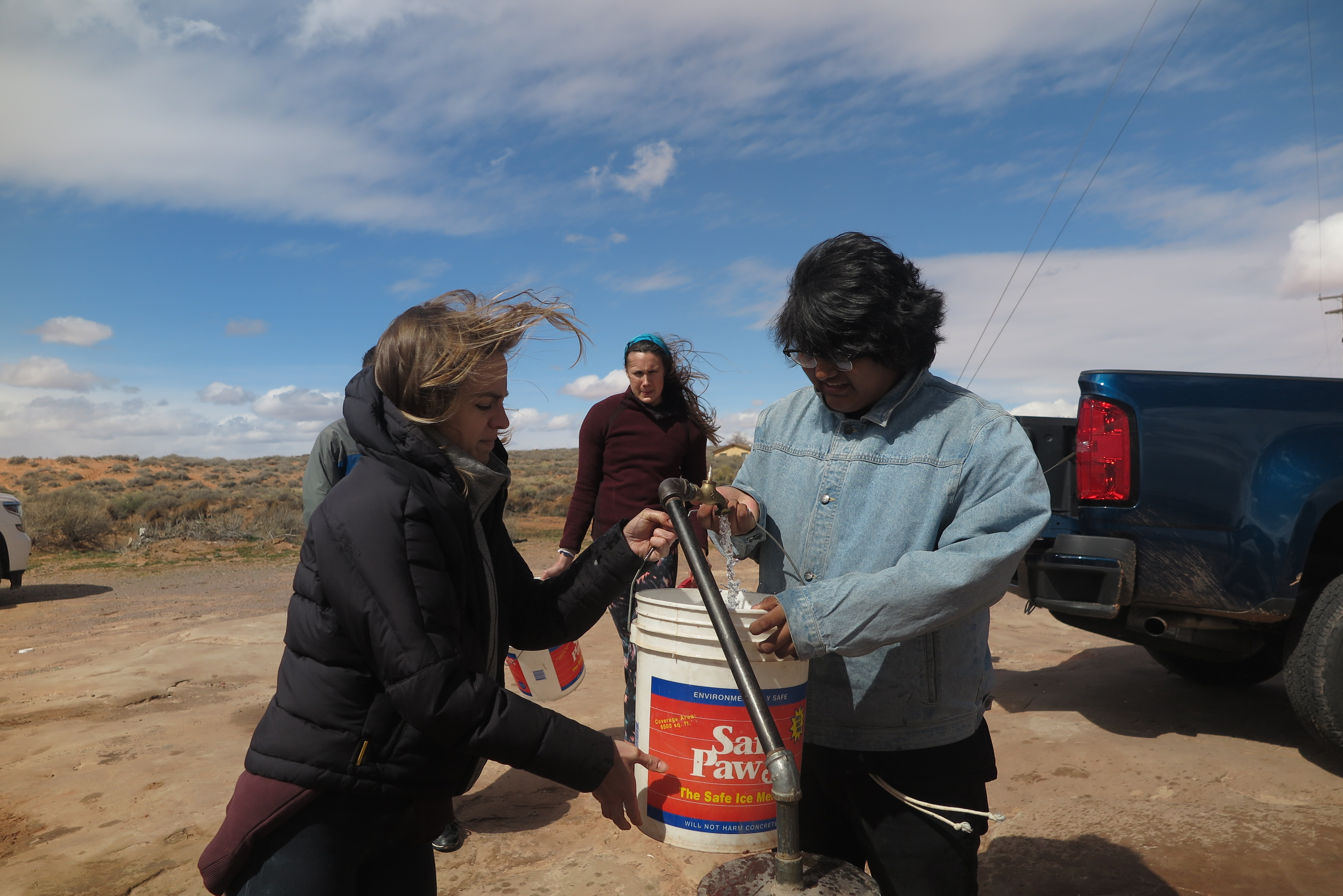 Graduate students in the Indige-FEWSS program fill buckets with well water and load them onto a pickup truck for use by a Diné family.