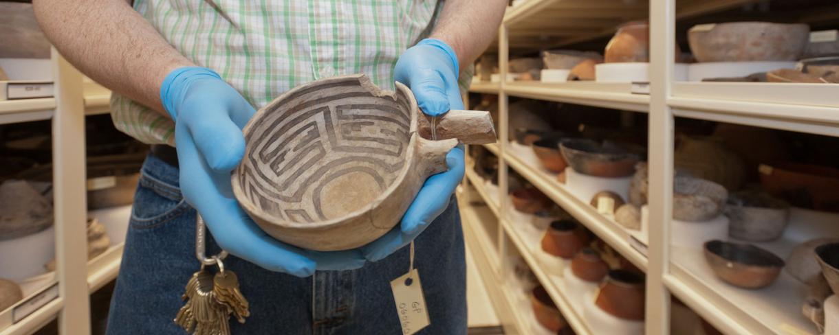 An art conservator is holding a native pot in the Arizona State Museum