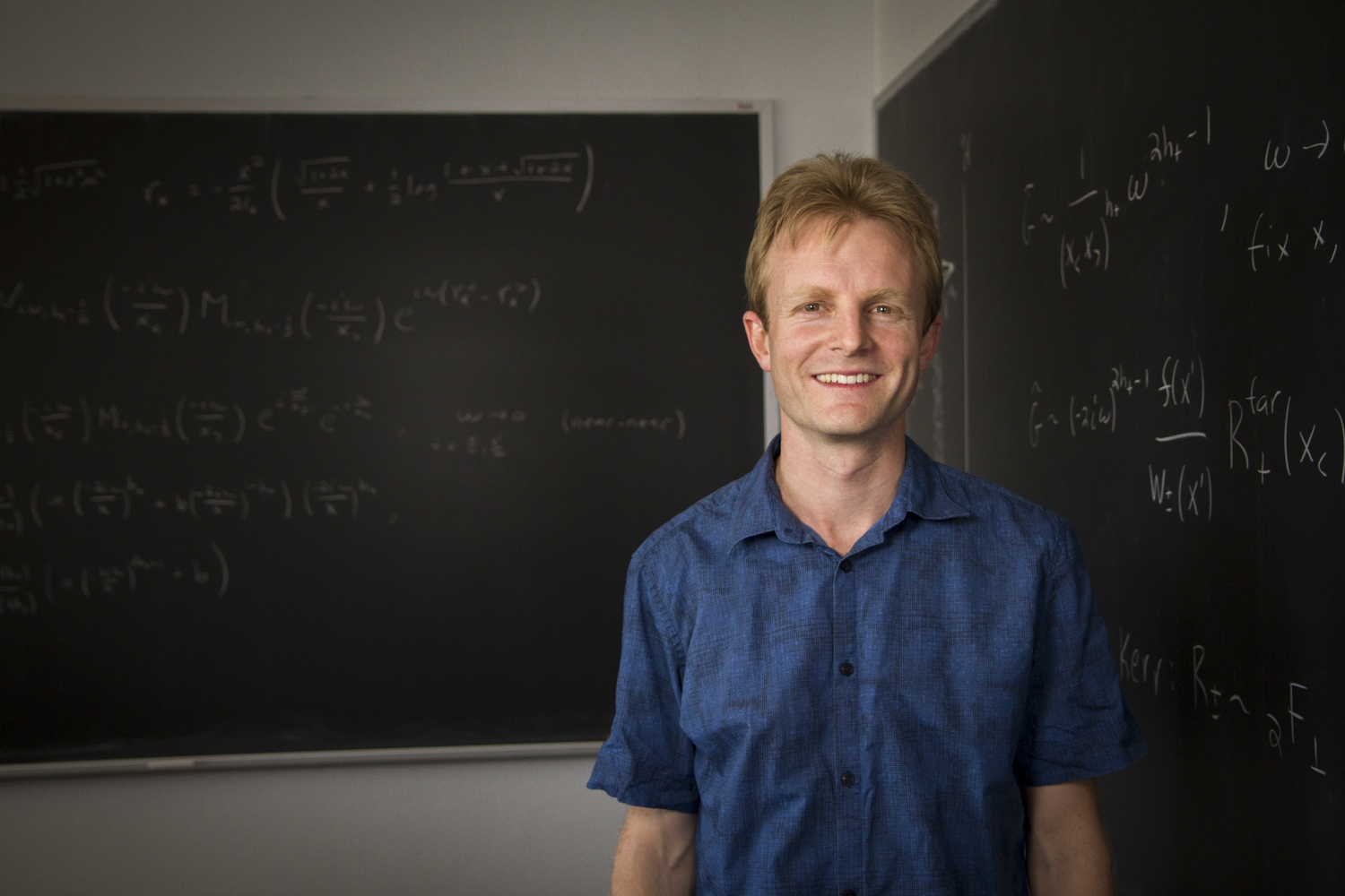 UA physicist Sam Gralla stands in front of two blackboards in his office.