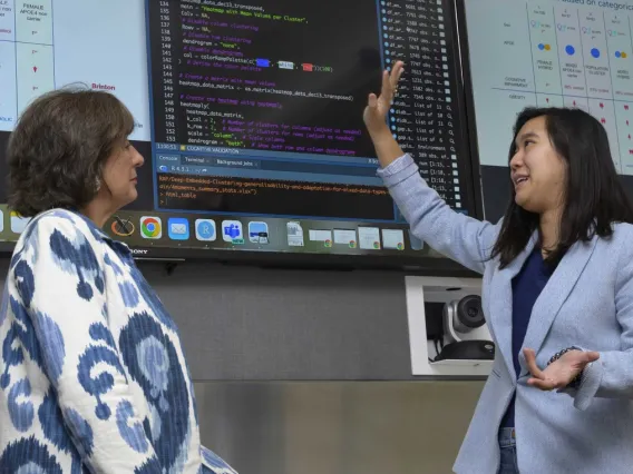 Two women discuss data below a set of monitors