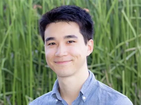 Image of smiling man in blue shirt in front of grassy background