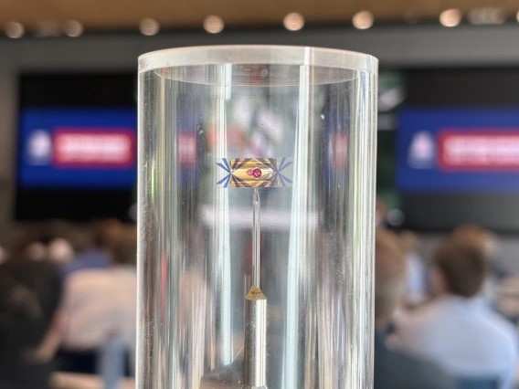 A glass tube holds a red ball inside a gold bar with blue streaks coming off of it.