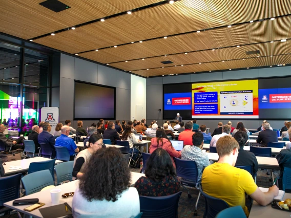 A crowded room full of seated people listening to a presentation.