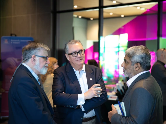 Three men speak in the lobby of the Grand Challenges Research Building.