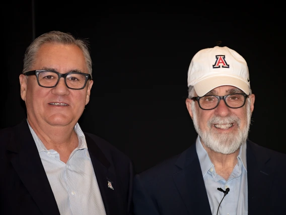 Two men in glasses pose for a picture in front of a black backdrop.