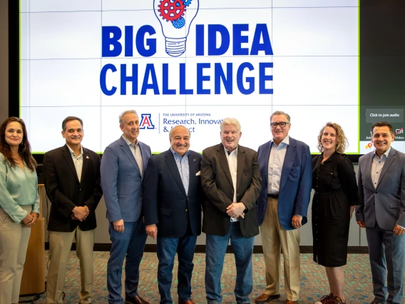 Smiling individuals standing shoulder-to-shoulder in front of a large screen that reads Big Idea Challenge