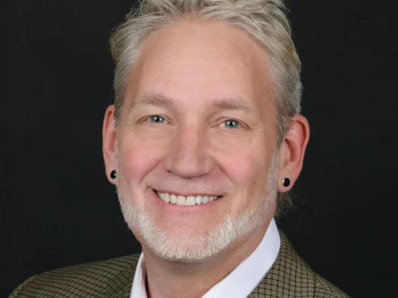Headshot of Ash Black wearing a white shirt and blazer in front of a solid black background