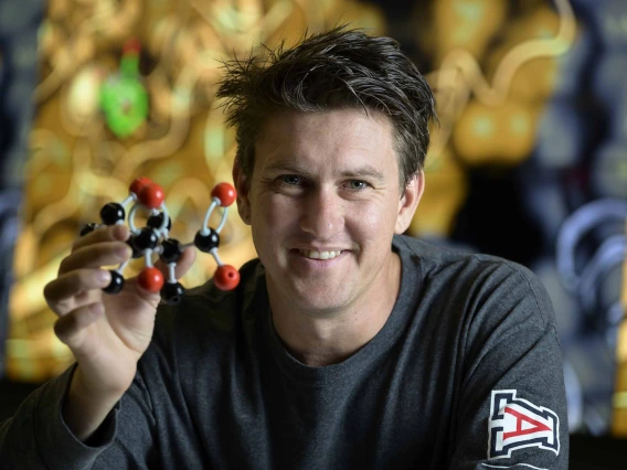A person holding a detailed model of a molecule represented by spheres connected by curved bars