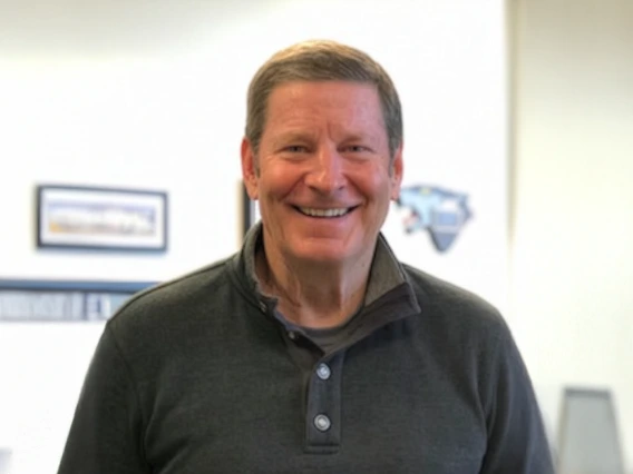A man in a green collared shirt smiles at the camera for a portrait.
