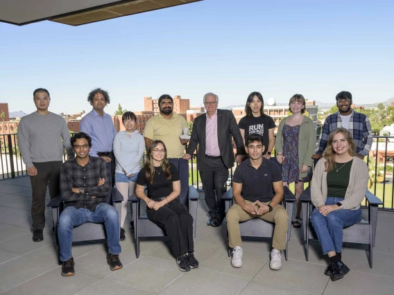Twelve people, most of whom are graduate students, sit and stand in a group on a balcony.