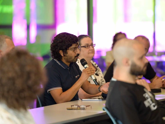 A man in an audience holds a microphone as he asks the presenter a question. 