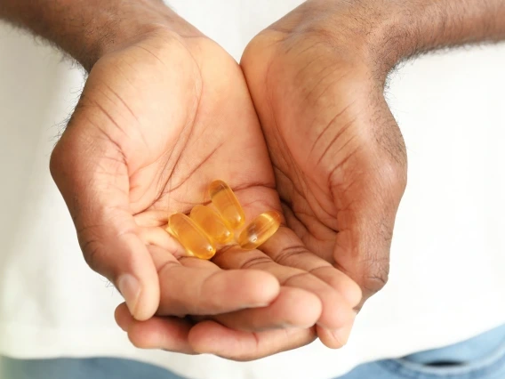 Close-up of a person holding several yellow softgel capsules in cupped hands, with a light green background. The image suggests a focus on health, wellness, or supplements.