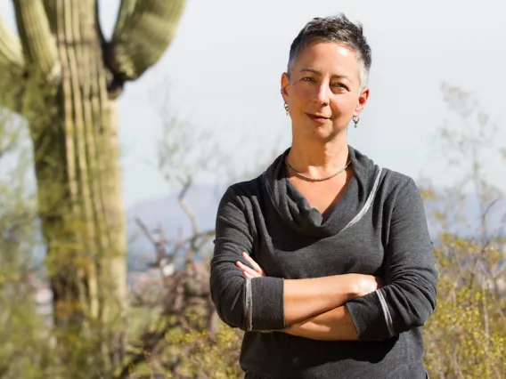 Tumamoc Arts Fellow Lyn Hart poses next to a Saguaro cactus.