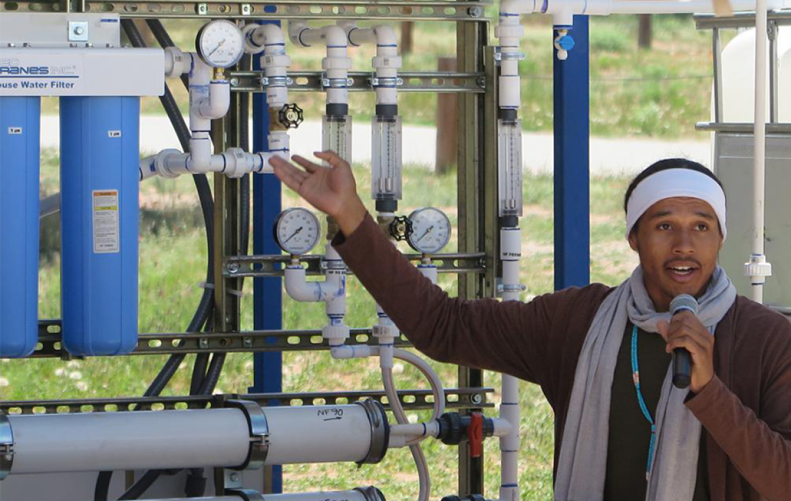 A researcher with a microphone gestures toward a water filtration system