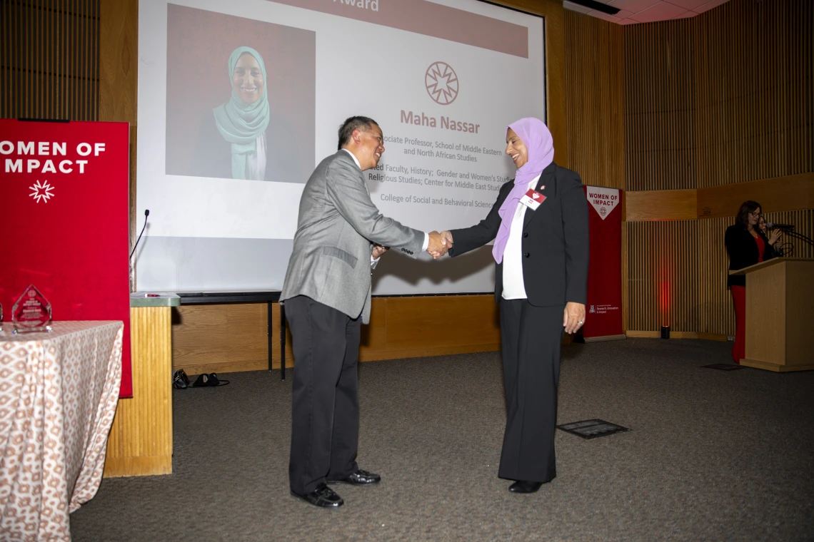 Two individuals shake hands in front of a projector screen.