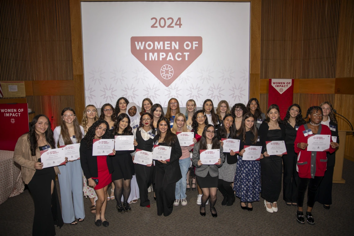 A group of young women holding their awards pose for a photo in front of a projector screen.