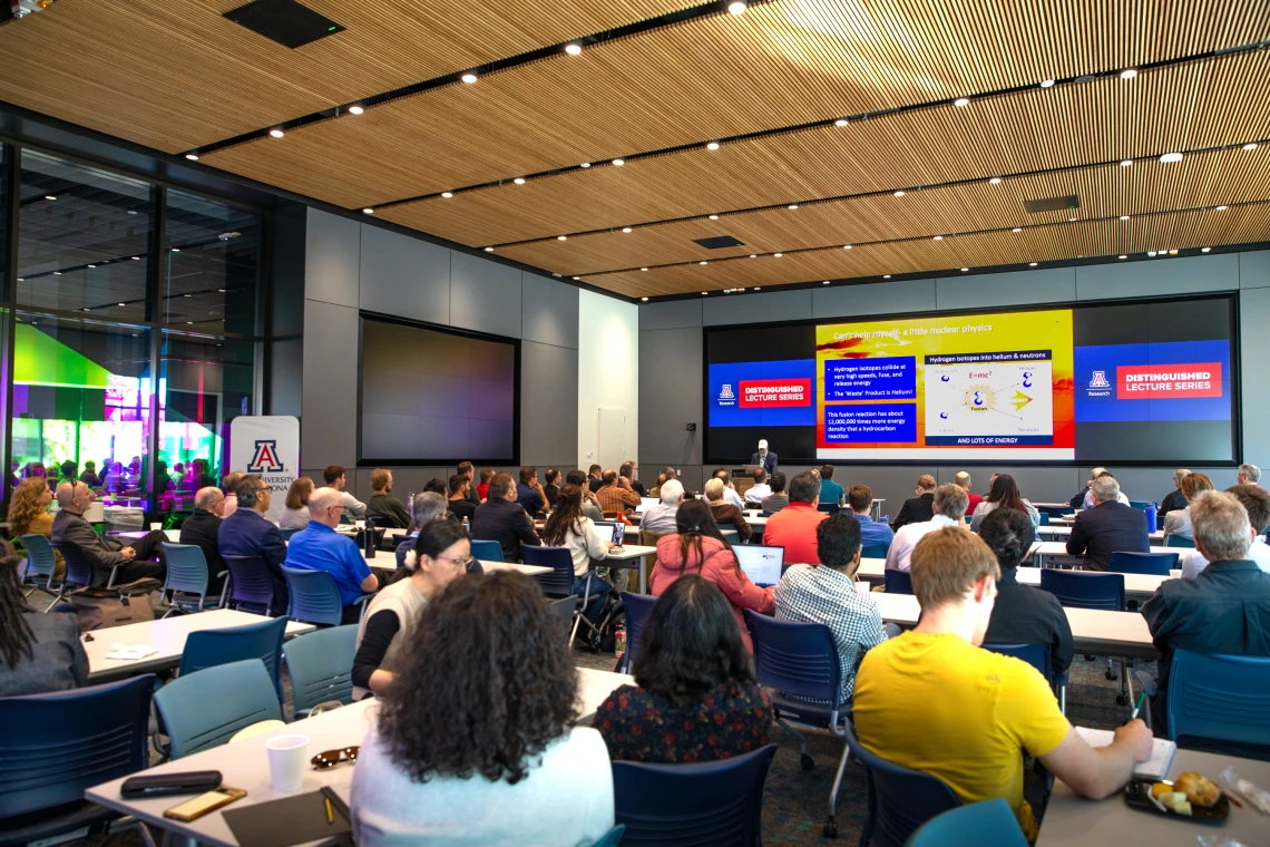 A crowded room full of seated people listening to a presentation.