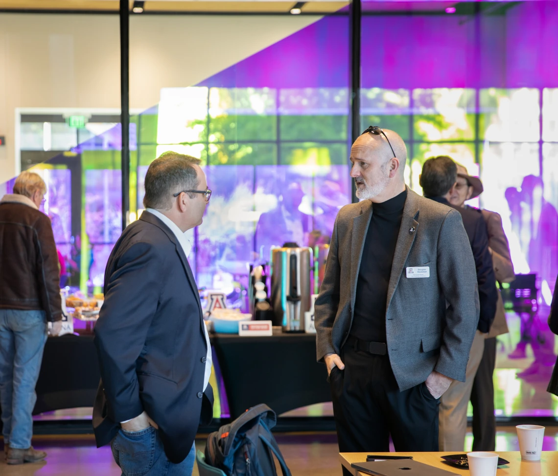 Men in blazers talk to each other in the lobby of the Grand Challenges Research Building.