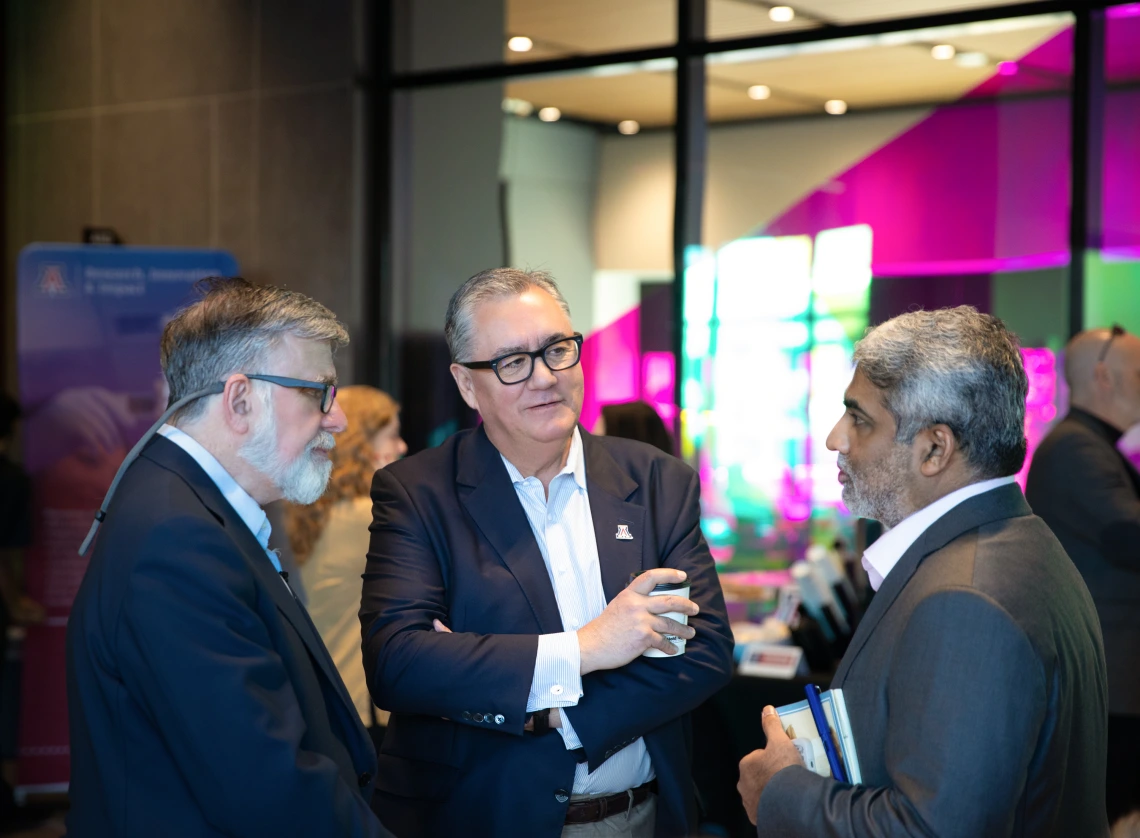 Three men speak in the lobby of the Grand Challenges Research Building.