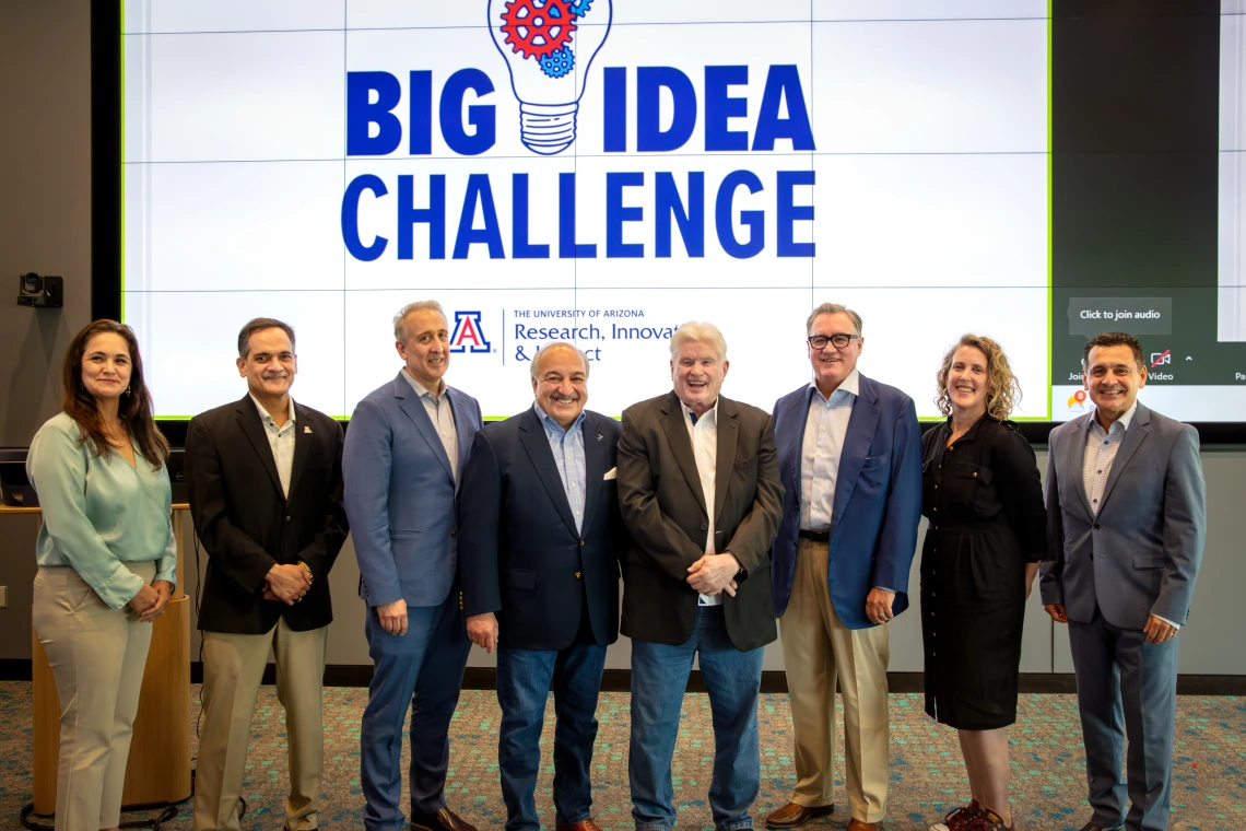 Smiling individuals standing shoulder-to-shoulder in front of a large screen that reads Big Idea Challenge