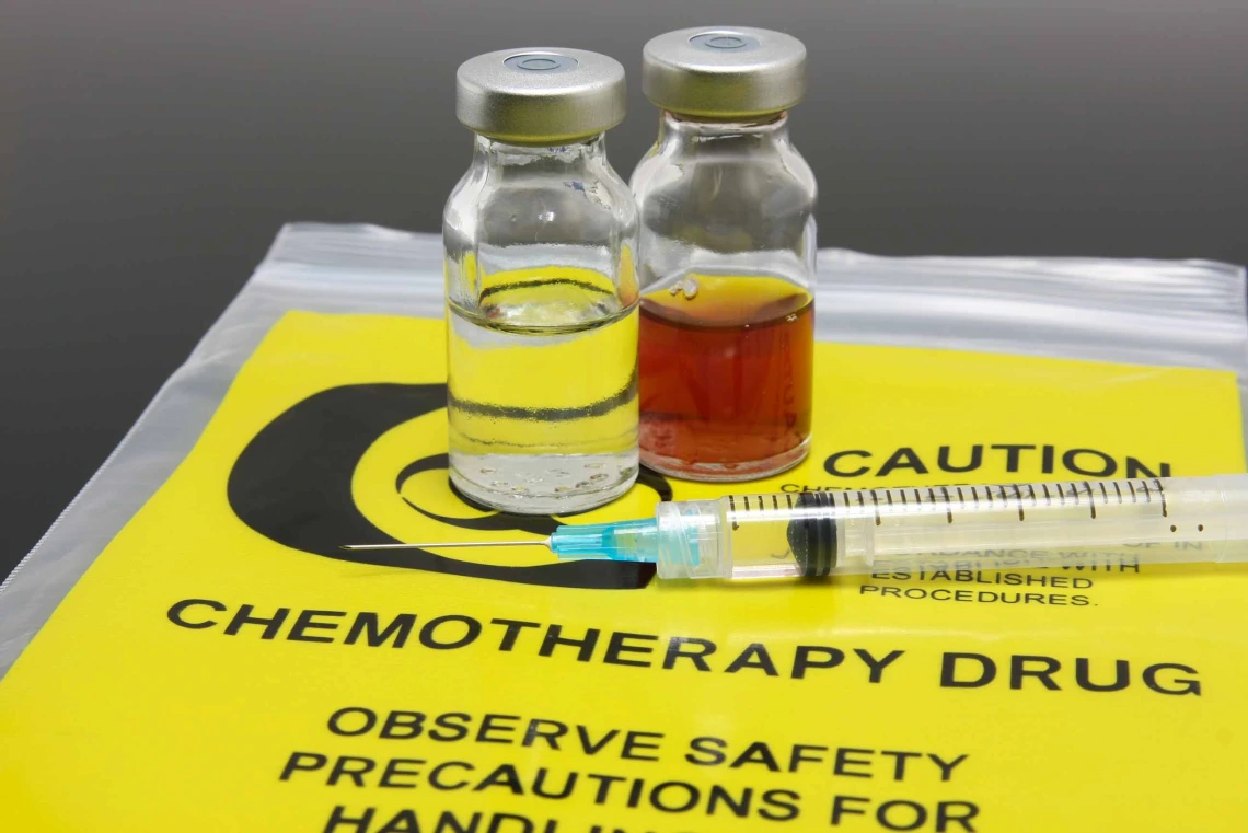 Two vials of liquid medication and a syringe on an empty yellow bag with black text “chemotherapy drug, observe safety precautions”