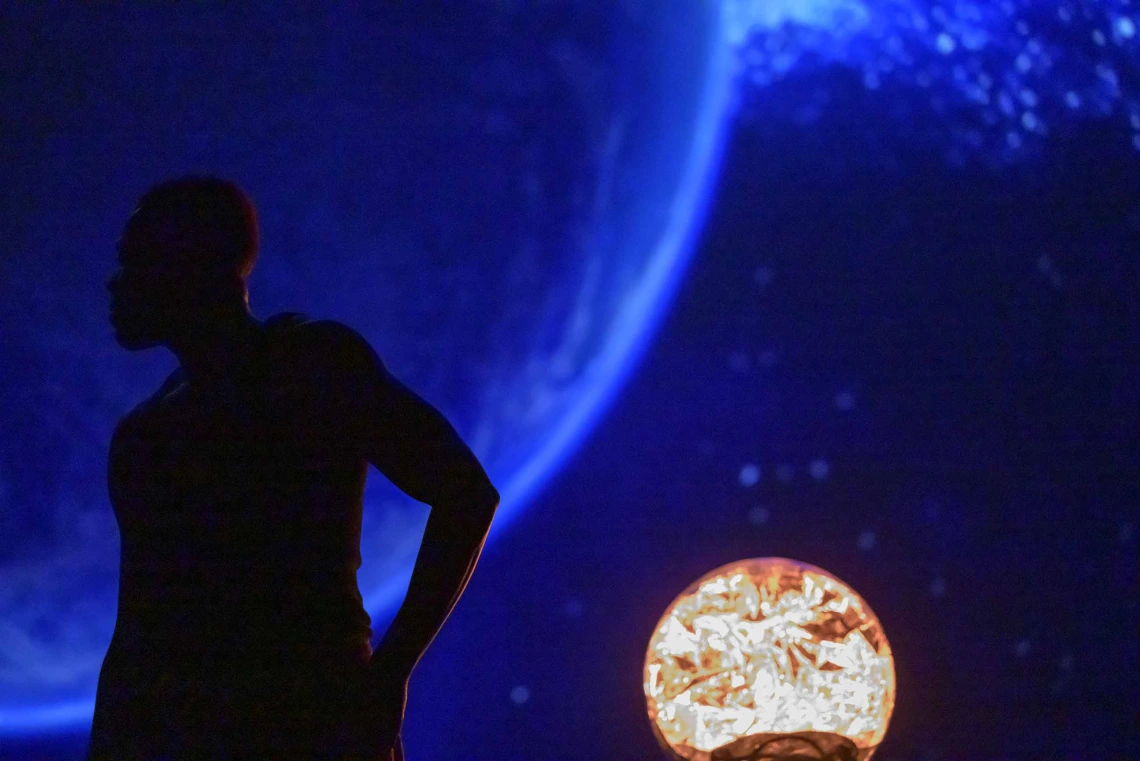 A dancer stands in silhouette in front of an image of space