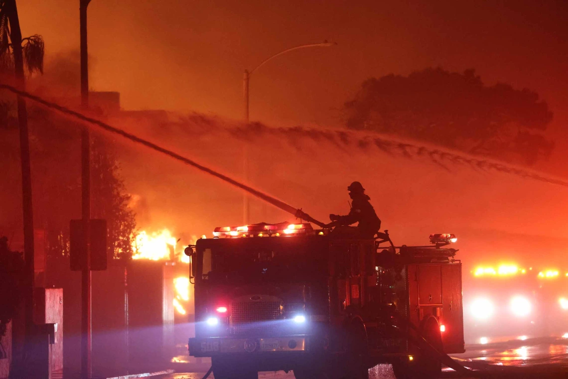 Firefighter on top of fire truck using hose to spray water on burning homes