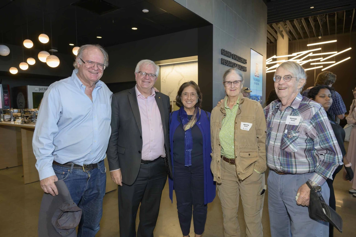 Five professors stand beside each other smiling during a reception. 