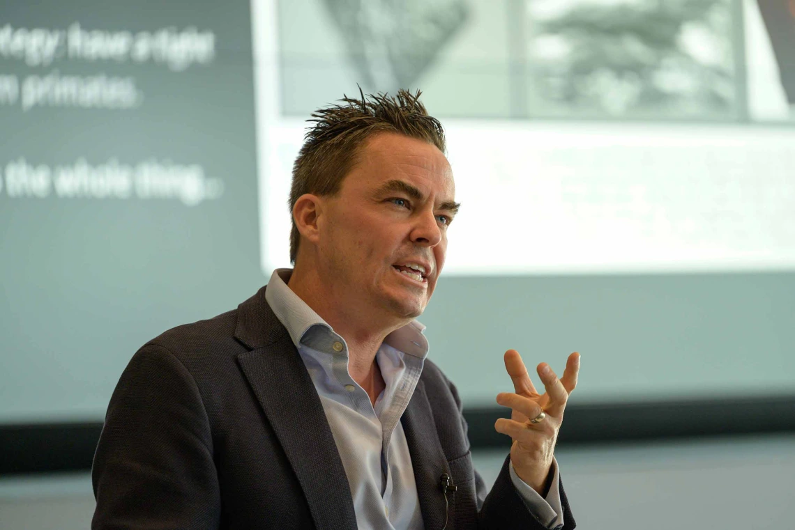 A man is talking intensely while a projection screen in the background 