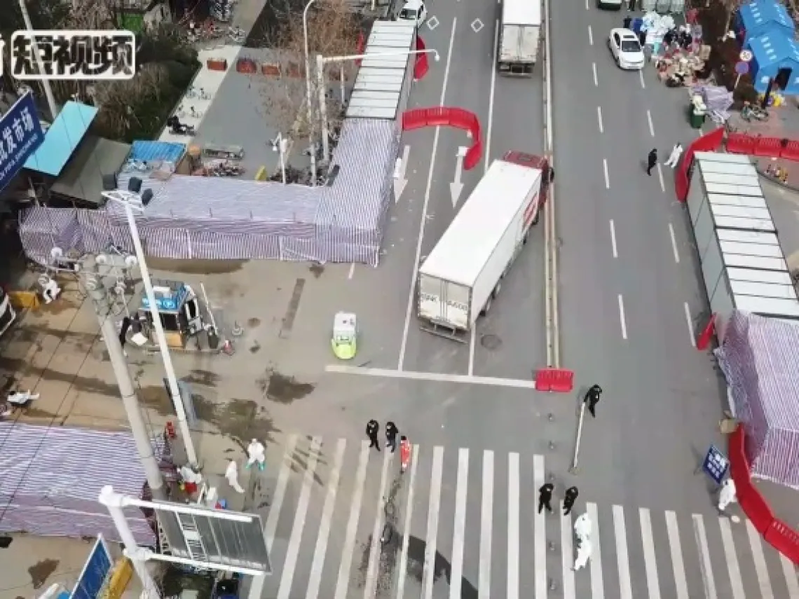 semi trucks and people wearing hazmat suits can be seen outside the main entrance to the Huanan Seafood Market in Wuhan, China