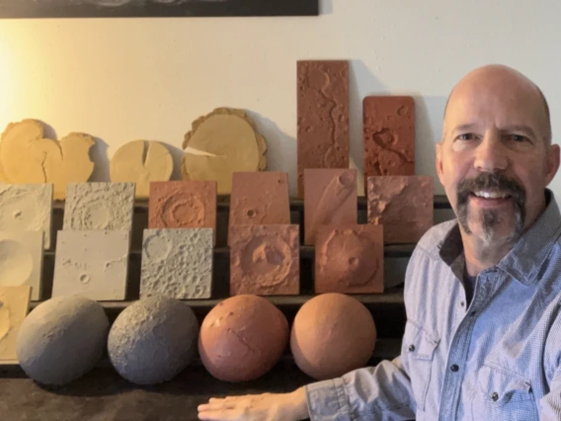 Steve Kortenkamp in front of a desk with lunar models of various colors