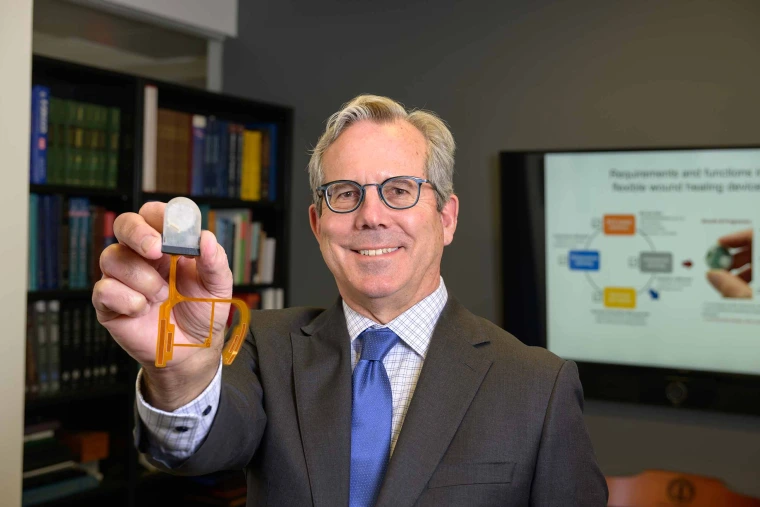 A person holds a small grey wearable device used for would healing