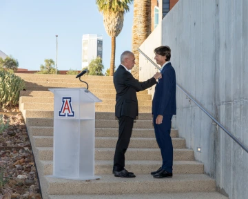 A man standing next to a podium with the block "A" places a pin onto another man.