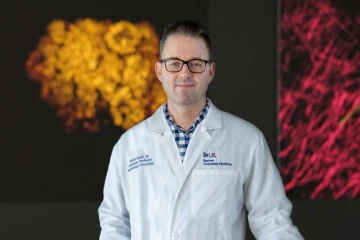 Portait of Dr. Aaron Scott wearing a white coat with scientific art in the background
