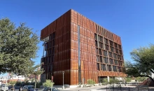 A large building sits between two trees under a clear, blue sky.