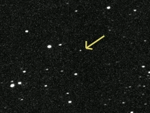An arrow points to a dot of light among a field of background stars