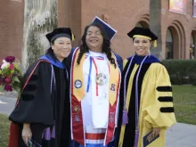 Angela Acuna, Sharon Hom and Timian Godfrey smiling and posing for a photo in caps and gowns