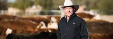 George Ruyle standing in the sun in front of a herd of cattle with his white cowboy hat on