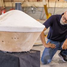A man crouches next to a replica of the flying saucer-like sample capsule.