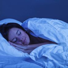 a person sleeping in a bed with white sheets under a soft blue light