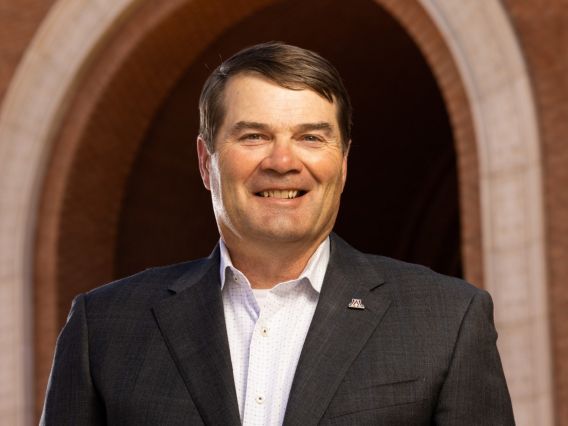 Gary Packard smiling, standing in front of a brick building and arched entry