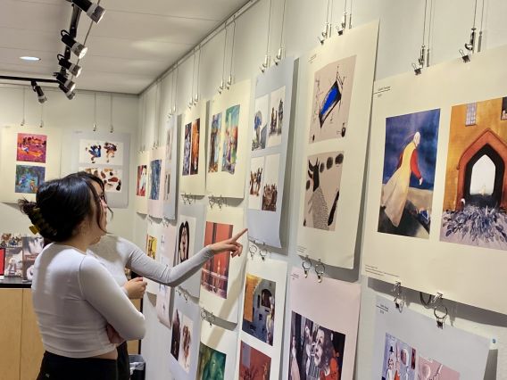 Two undergraduate women look at illustrated book proofs displayed on a wall