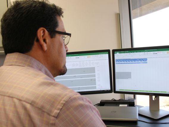 A man wearing glasses sits at a computer and is visible in profile