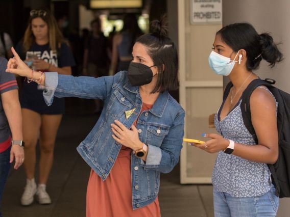 a woman wearing a mask points while another one woman in a mask looks in that direction