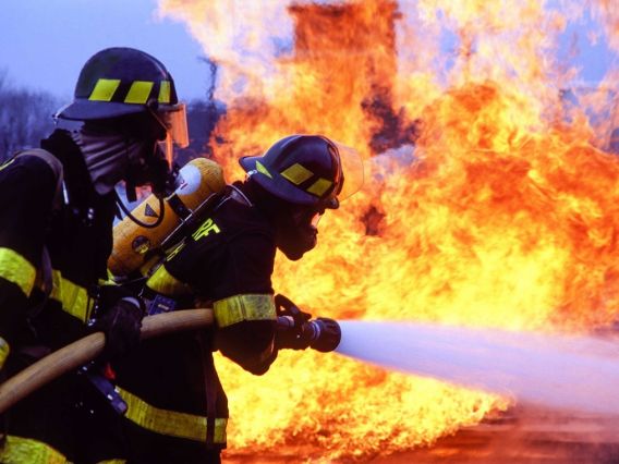 Two firefighters work to extinguish a large fire.
