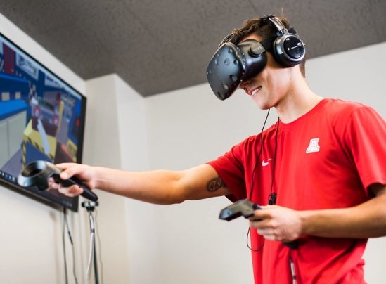 UArizona student smiles while using a virtual reality headset and hand controller