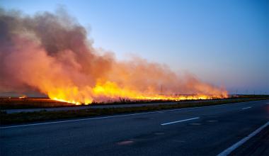 wildfire burning in a field near an empty highway road