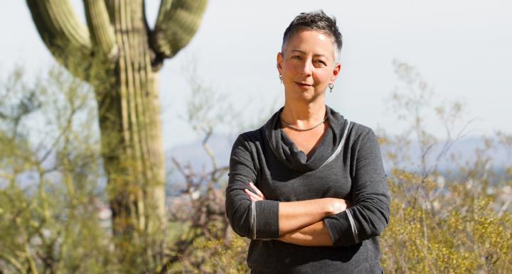 Tumamoc Arts Fellow Lyn Hart poses next to a Saguaro cactus.