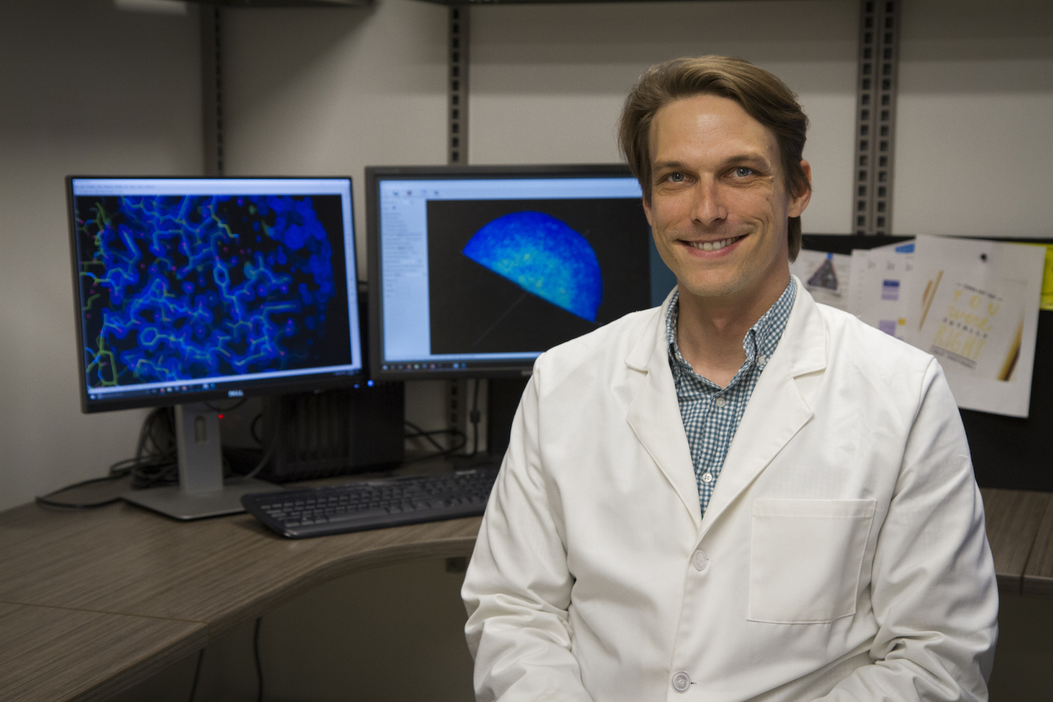 Thomas Moon sits in front of two computer screens in the lab.